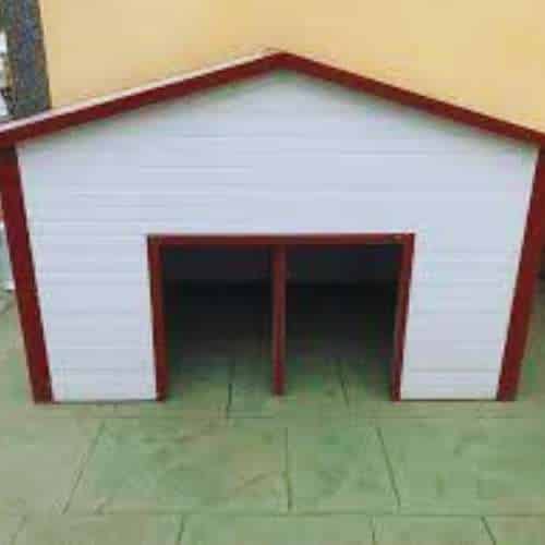 Caseta de perro doble con diseño de madera blanca y bordes rojos ubicada en un patio exterior.