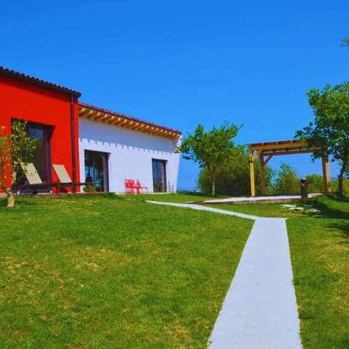 Instalaciones modernas de la Residencia Canina Kanoteka en Bilbao, con un edificio rojo y blanco rodeado de césped verde y un cielo despejado.
