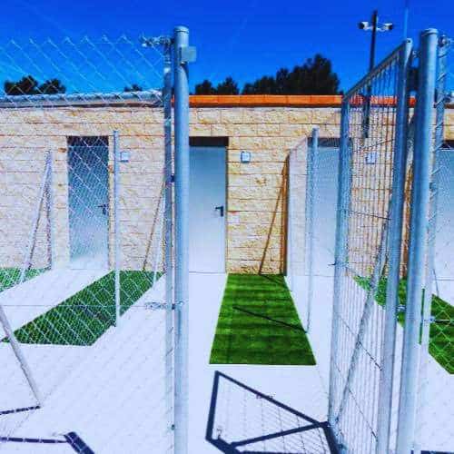 Instalaciones modernas de la Residencia Canina Las Cortes en Burgos, con jaulas individuales, césped artificial y un edificio de piedra bajo un cielo despejado.