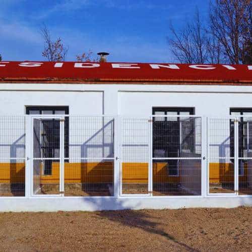 Vista exterior de las instalaciones de la residencia canina Los Álamos en Toledo, con jaulas espaciosas y área de entrada iluminada.