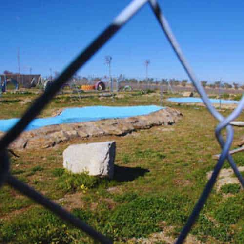 Vista a través de una cerca de la zona recreativa en la residencia canina Territorio Canino en Toledo, que incluye áreas de césped y una piscina para mascotas.